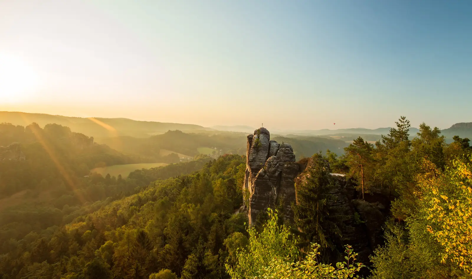 Gegenlicht über dem dunstigen Tal, eine einzelne Felsnadel hebt sich als Silhouette ab.