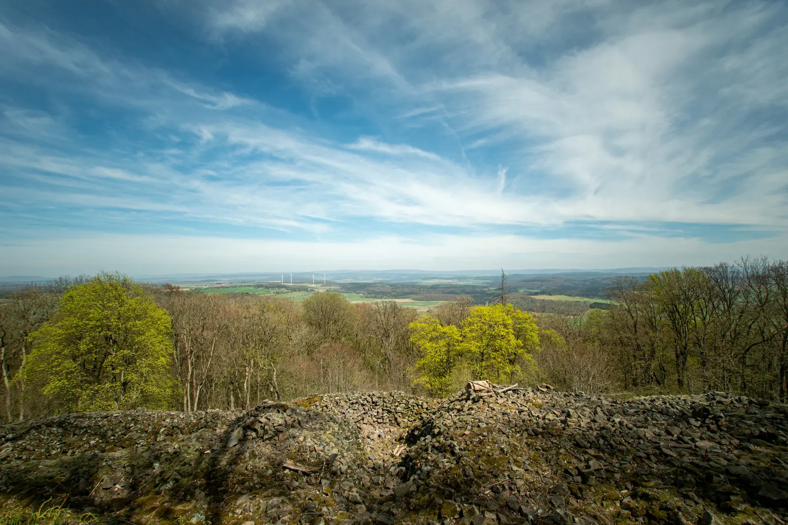 Weiter Blick über bewaldete Hügel, Wolkenstreifen am blauen Himmel.