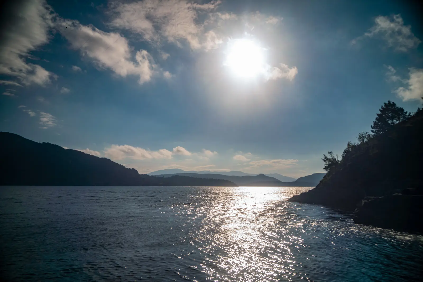 Gegenlicht über einem Fjord, die Sonne spiegelt sich auf der Wasseroberfläche.