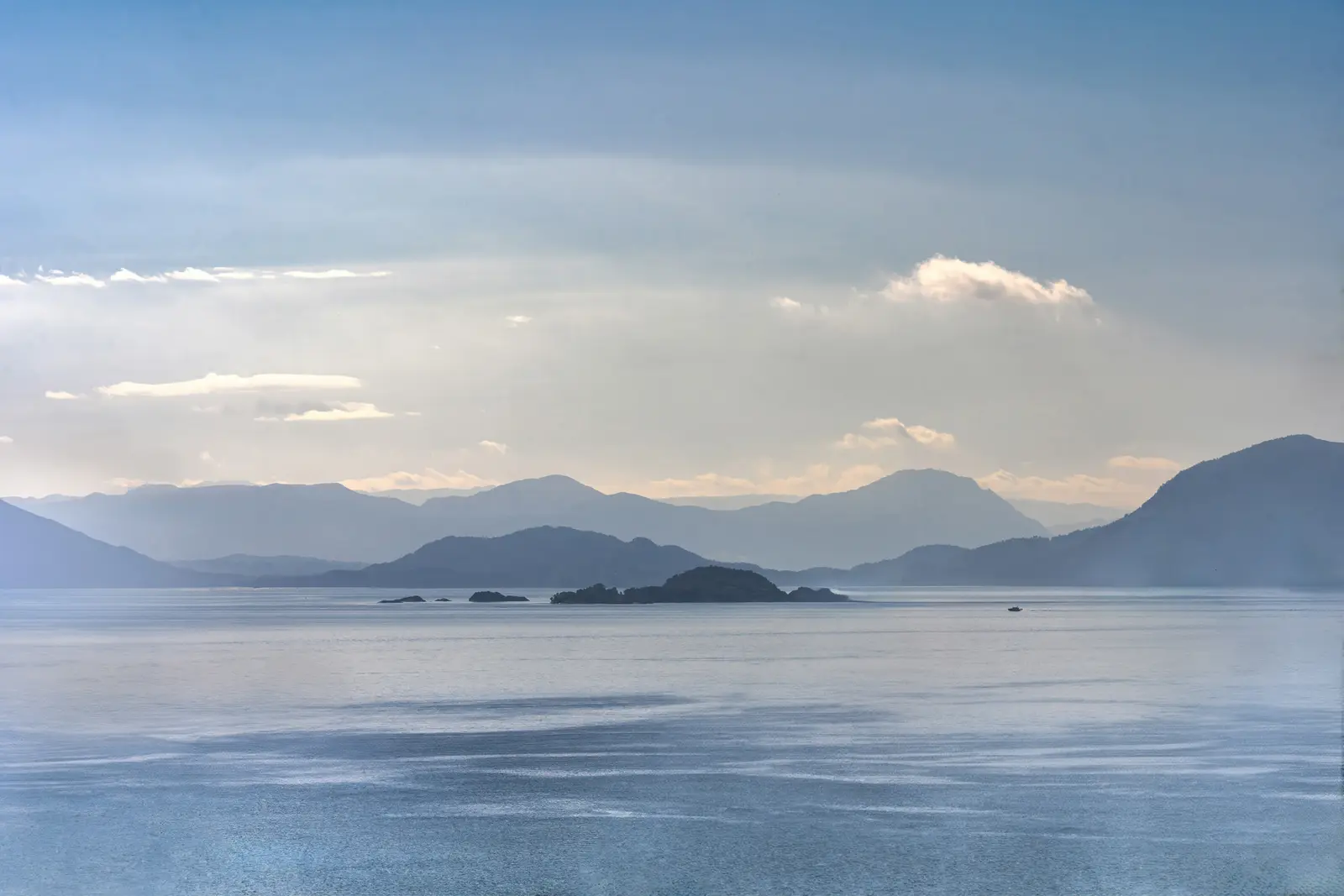 Diesige Fjordlandschaft, die Bergketten staffeln sich hinter dem Wasser.