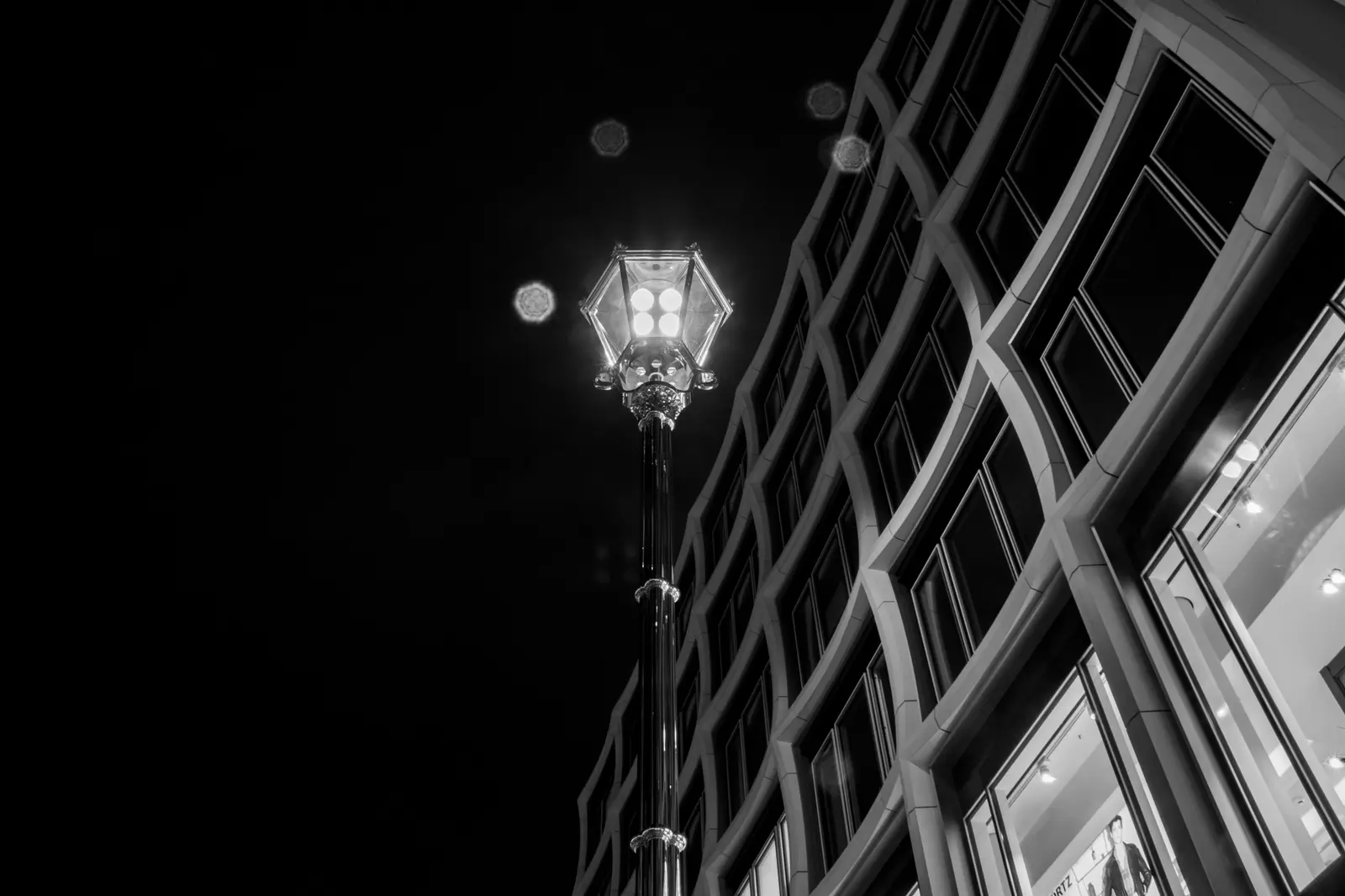 Schwarzweiß: geschwungene Glasfassade und eine Straßenlaterne bei Nacht.