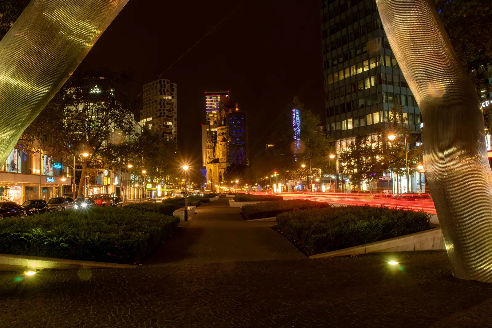 Nächtliche Straße mit Lichtspuren zwischen beleuchteten Hochhäusern.