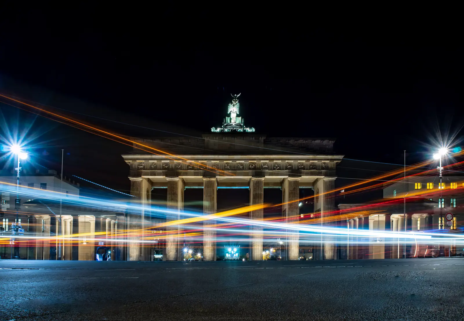 Brandenburger Tor bei Nacht, davor die Lichtspuren vorbeifahrender Fahrzeuge.