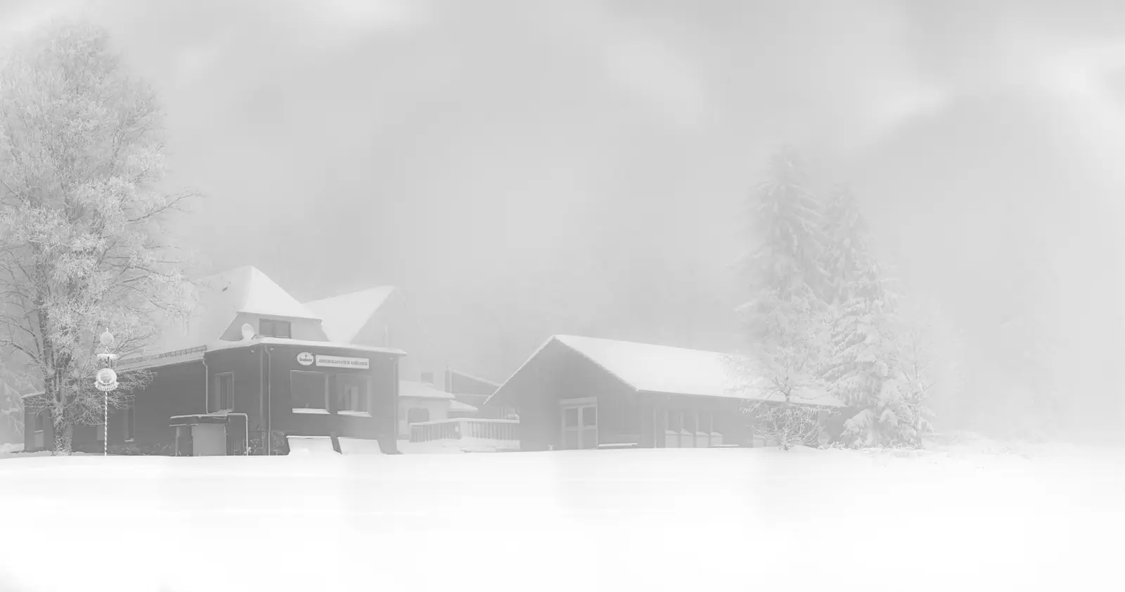 Gebäude am verschneiten Ufer, in dichten Nebel gehüllt.